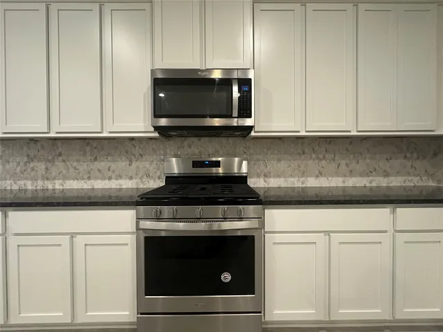 a kitchen with stainless steel appliances granite countertop white cabinets and a stove top oven