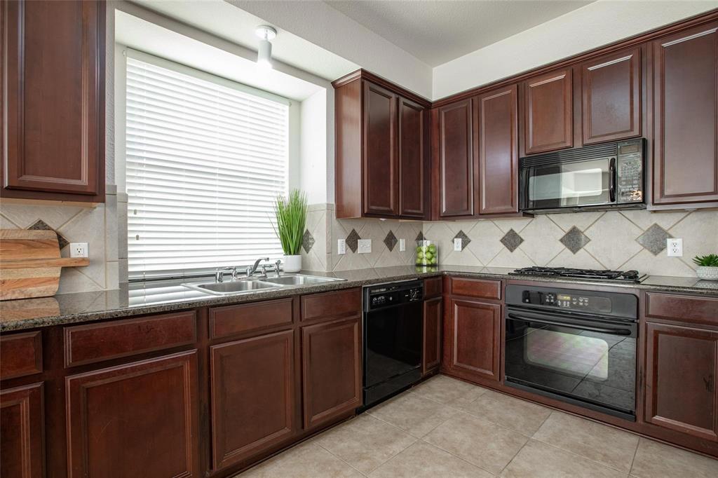 9305 Amber Downs Drive McKinney, TX 75072 - Photo 3 of 28 a kitchen with granite countertop wooden cabinets a stove top oven and sink