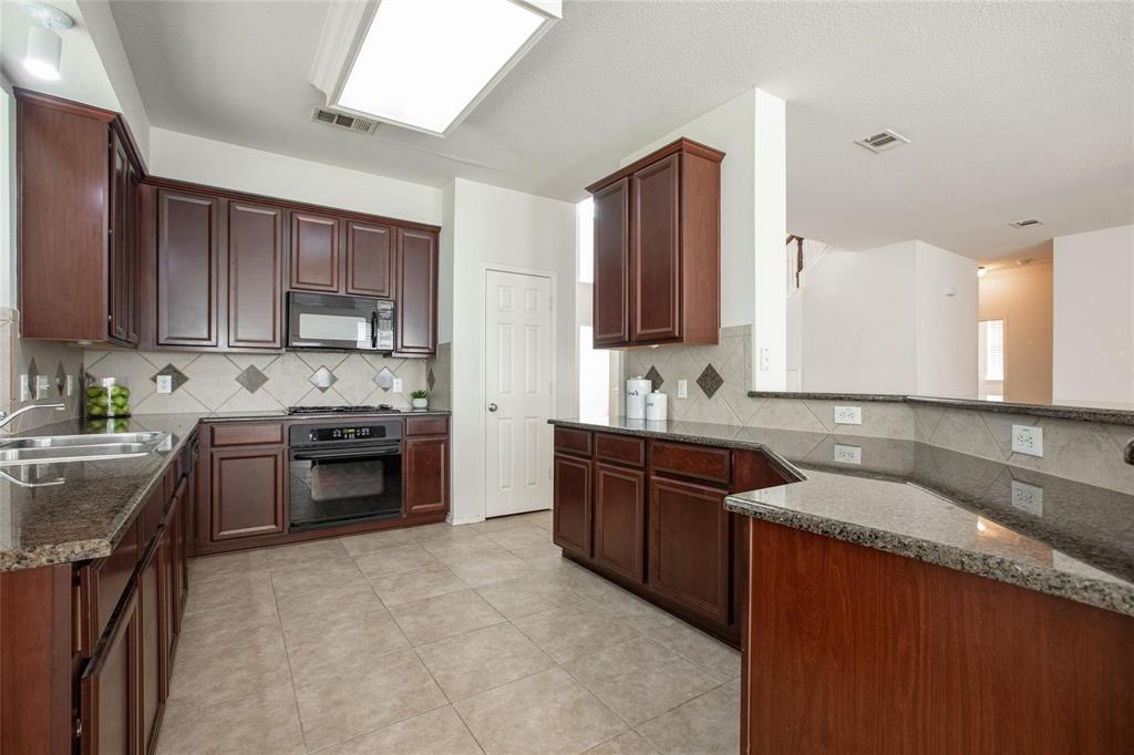 9305 Amber Downs Drive McKinney, TX 75072 - Photo 4 of 28 a large kitchen with granite countertop a sink a stove a oven a counter space and cabinets