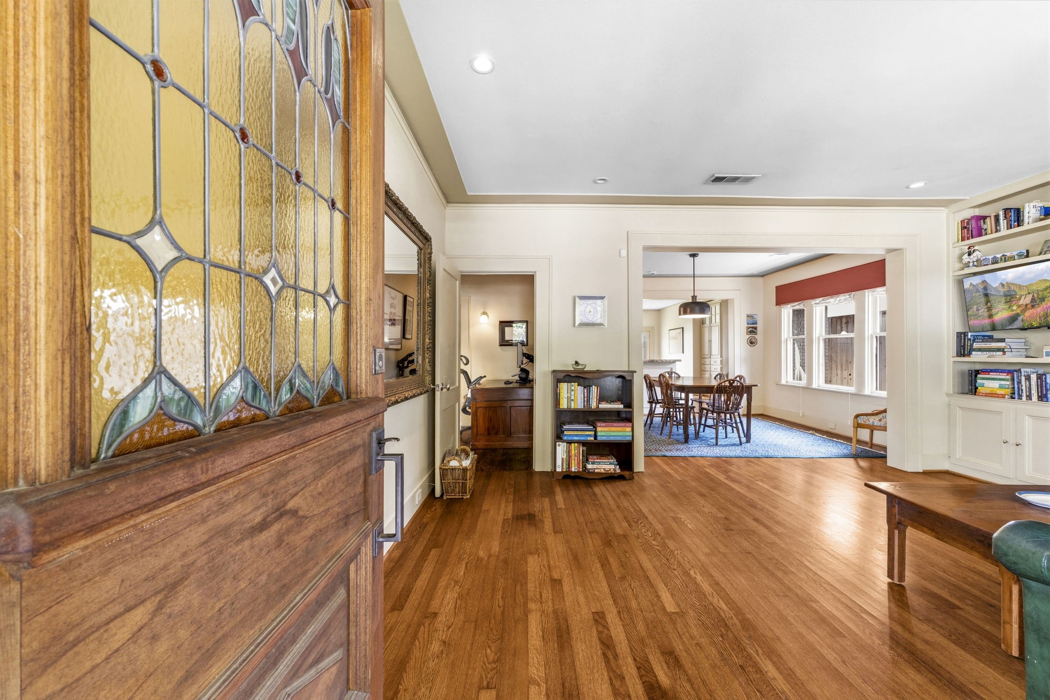 1521 Kipling Street Houston, TX 77006 - Photo 8 of 35 This welcoming home features a beautiful stained glass entry door, leading to a spacious living area with hardwood floors. It opens into a bright dining room highlighted by large windows and built-in shelves, creating a warm and inviting atmosphere.