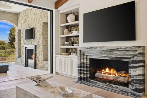 a living room with a fireplace a flat screen tv and a floor to ceiling window