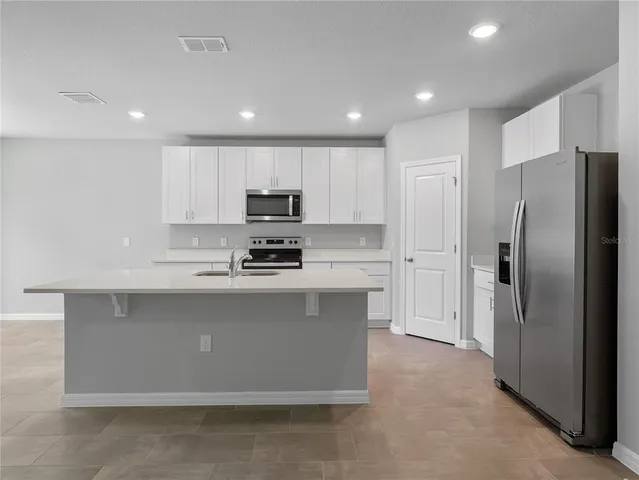 a large white kitchen with a stove a sink a refrigerator and white cabinets