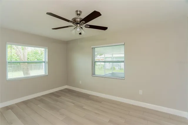 an empty room with wooden floor fan and windows