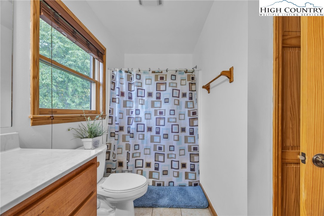 98 New Ridge Lane Piney Creek, NC 28663 - Photo 28 of 50 a bathroom with a granite countertop toilet a sink a mirror a window and a shower