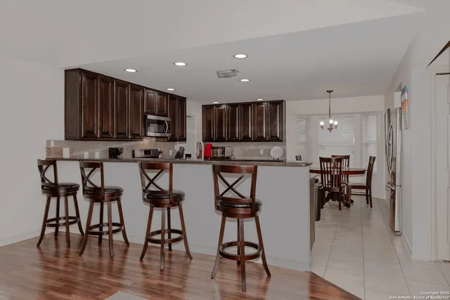 a open kitchen with stainless steel appliances granite countertop a stove top oven a dining table and chairs with wooden floor