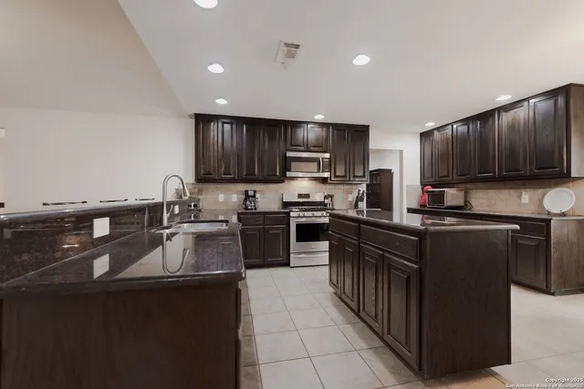 a kitchen with kitchen island granite countertop a sink dishwasher stove and refrigerator with wooden cabinets