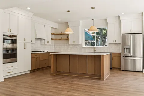 a kitchen with stainless steel appliances granite countertop a refrigerator a sink dishwasher a stove and white cabinets with wooden floor