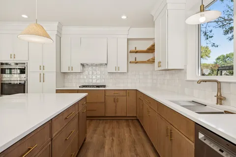 a kitchen with a sink dishwasher a stove top oven a refrigerator with white cabinets and wooden floor