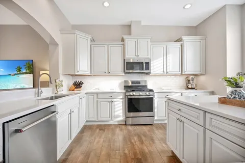 a kitchen with stainless steel appliances white cabinets a sink dishwasher a stove top oven a refrigerator with white cabinets and wooden floor