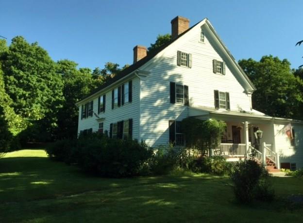 a view of a white house next to a yard with plants and trees