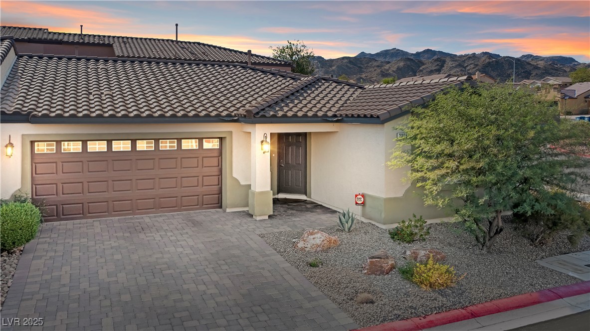 View of front of home with stucco siding, decorative driveway, an attached garage, and a tile roof