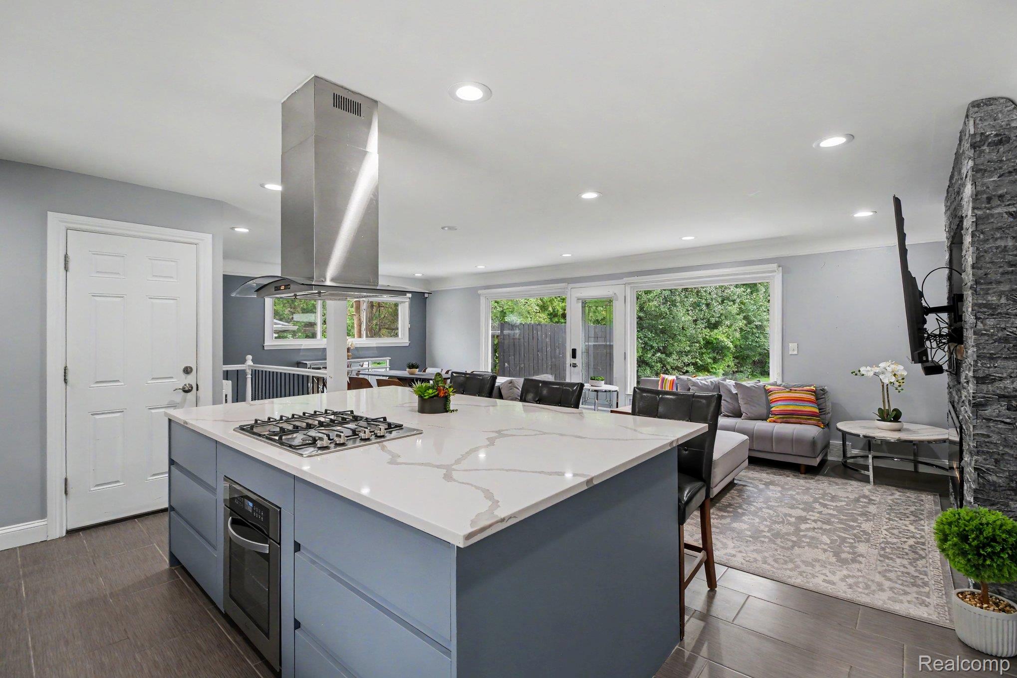 Kitchen island with a built-in cooktop, stainless steel range hood, white countertop, and integrated oven