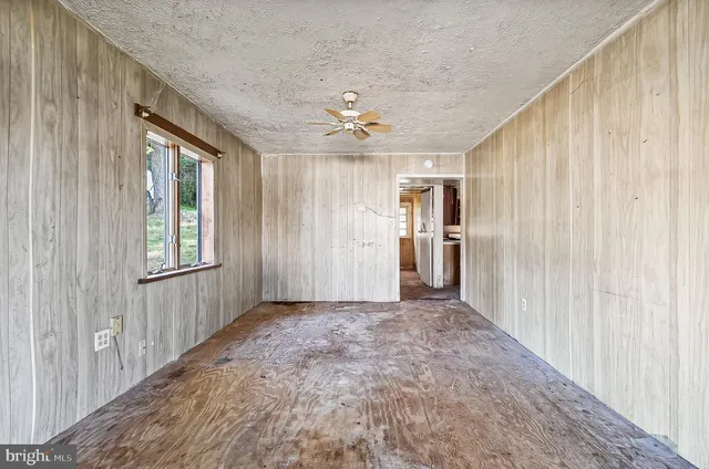 an empty room with chandelier fan and windows