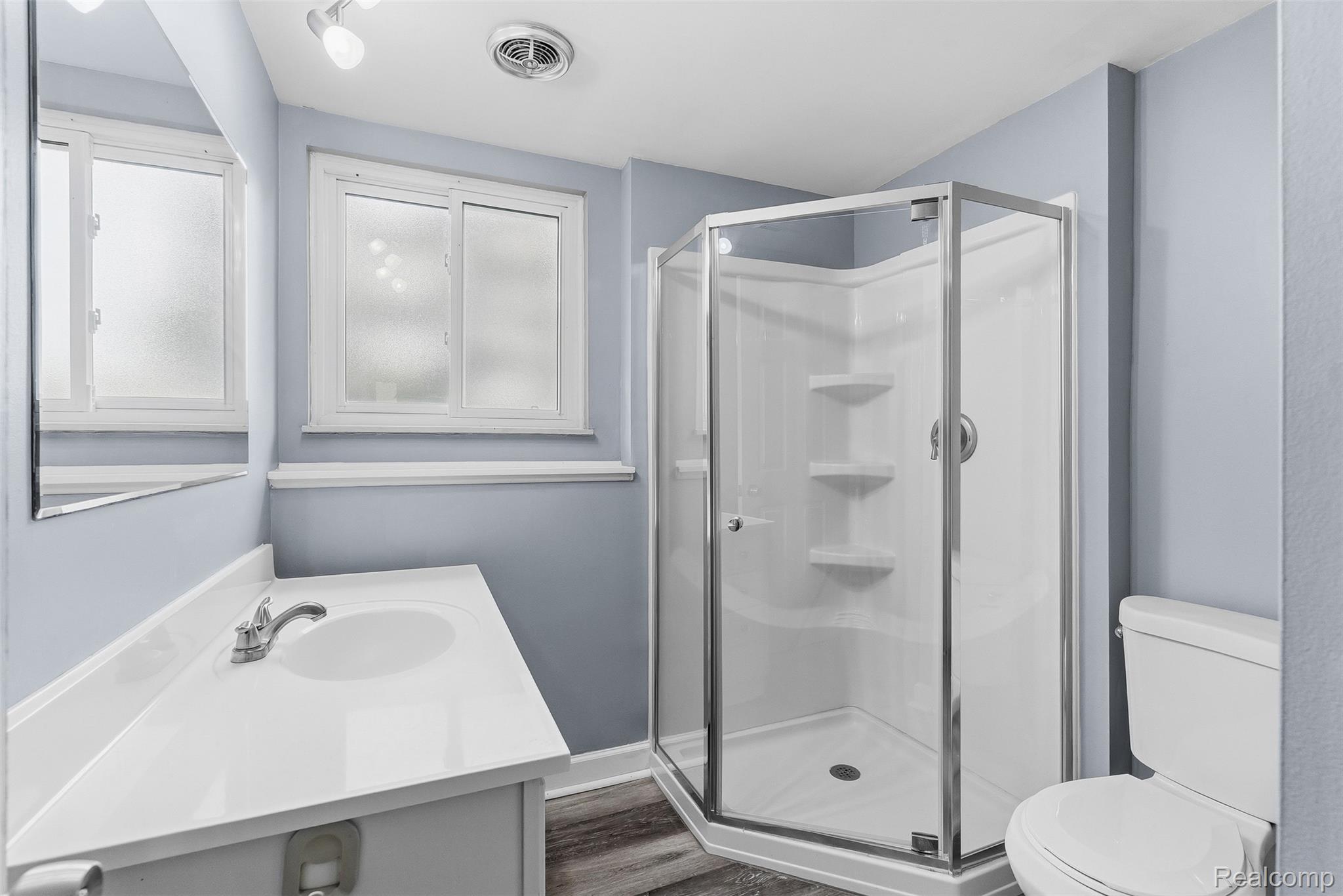 819 Alpine Trail Fenton, MI 48430 - Photo 26 of 41 Updated bathroom featuring a corner shower enclosure with glass doors and shelving, a white pedestal sink with chrome fixtures, a white toilet, light blue wainscoting, and recessed ceiling lighting