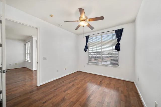 an empty room with wooden floor chandelier fan and windows