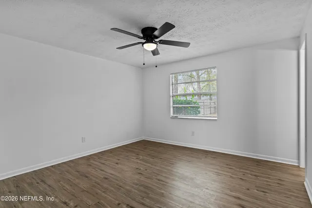 a view of an empty room with wooden floor fireplace and a window