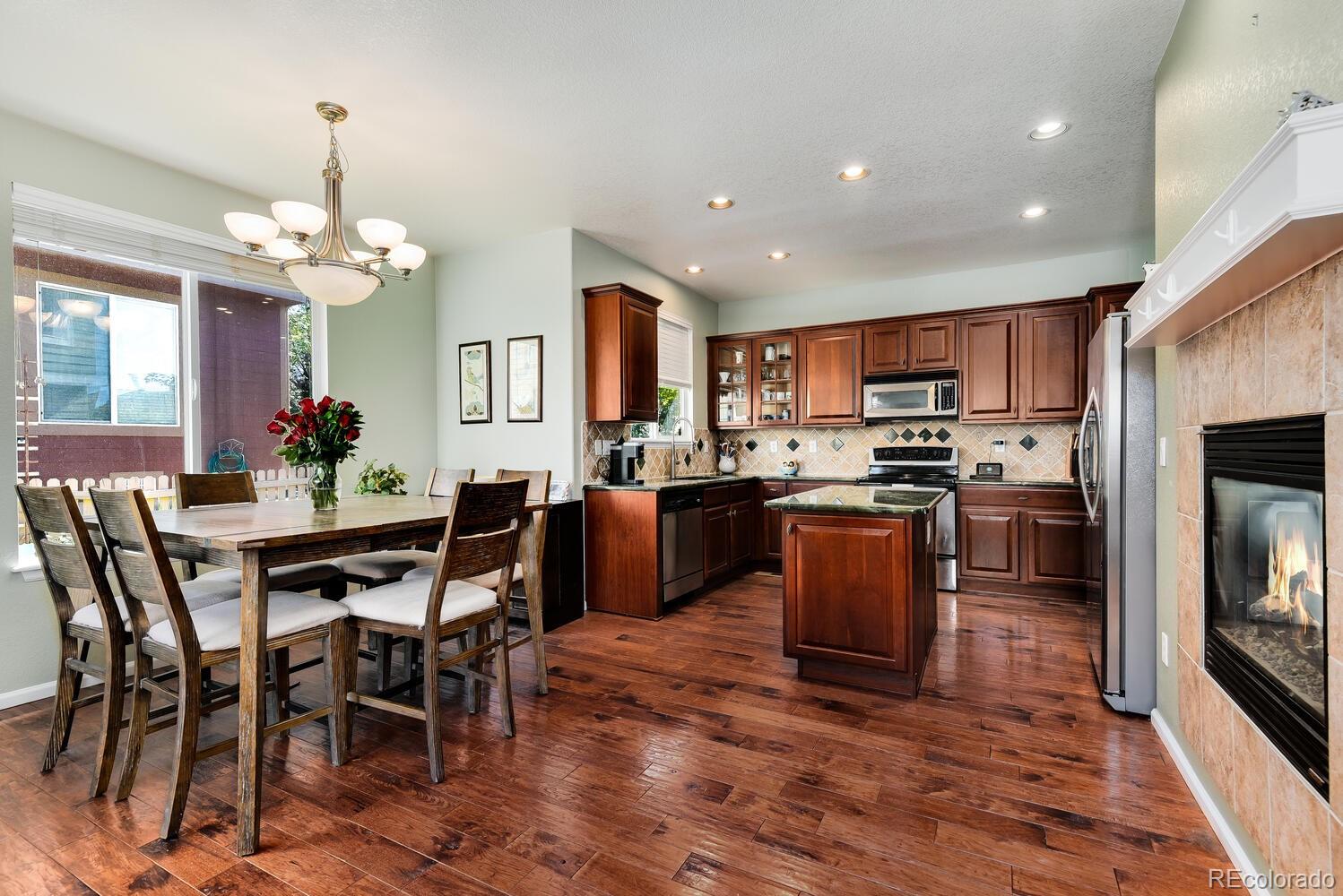 10842 Brooklawn Road Highlands Ranch, CO 80130 - Photo 11 of 35 a kitchen with kitchen island granite countertop wooden floors a stove a microwave a dining table and chairs