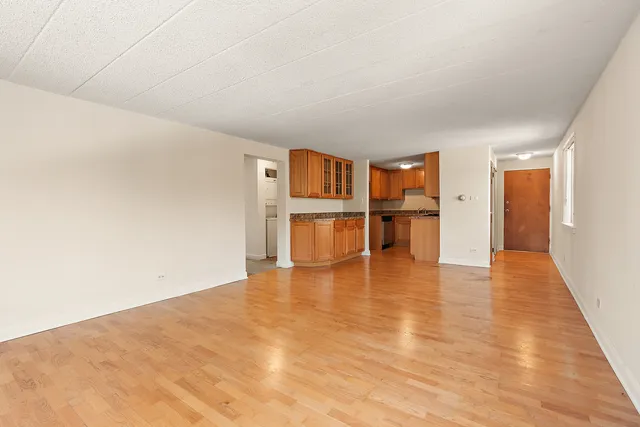 a view of empty room with wooden floor and a kitchen
