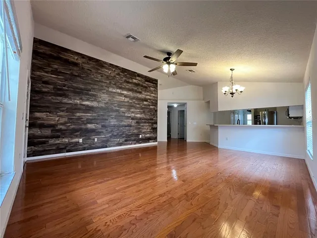 a view of an empty room with wooden floor and a ceiling fan