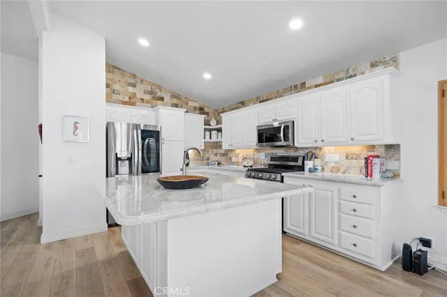 a kitchen with stainless steel appliances kitchen island granite countertop a refrigerator oven a sink dishwasher and white cabinets with wooden floor