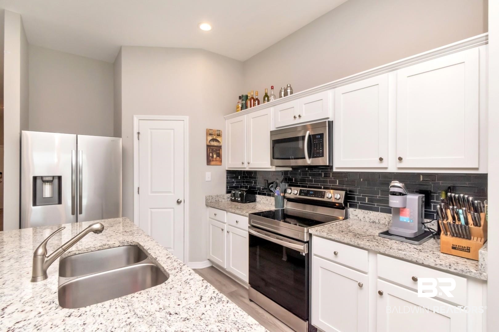 1295 Hayward Loop Foley, AL 36535 - Photo 11 of 29 Kitchen featuring a double stainless steel sink, granite countertops, white cabinetry, a black subway tile backsplash, and stainless steel appliances including a refrigerator, range, and microwave