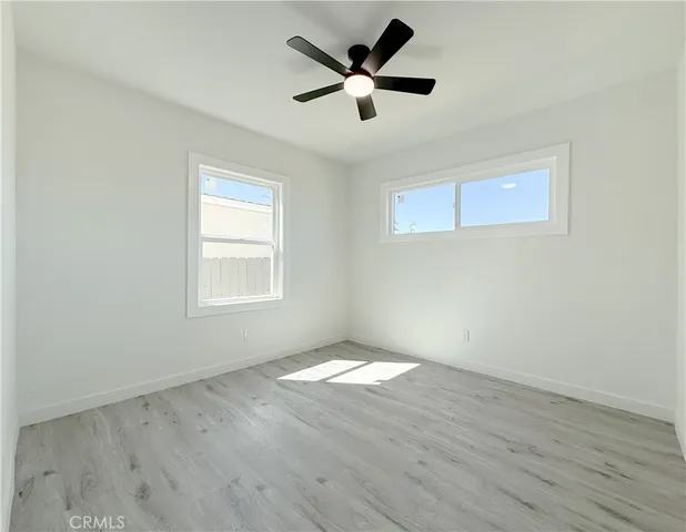 a view of an empty room with wooden floor and a ceiling fan