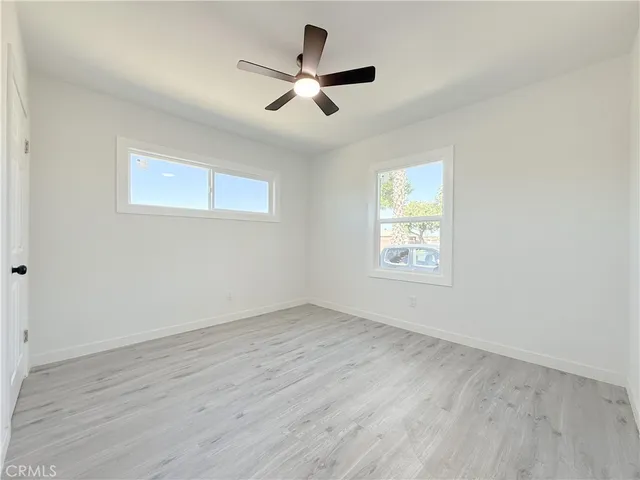 an empty room with wooden floor ceiling fan and window