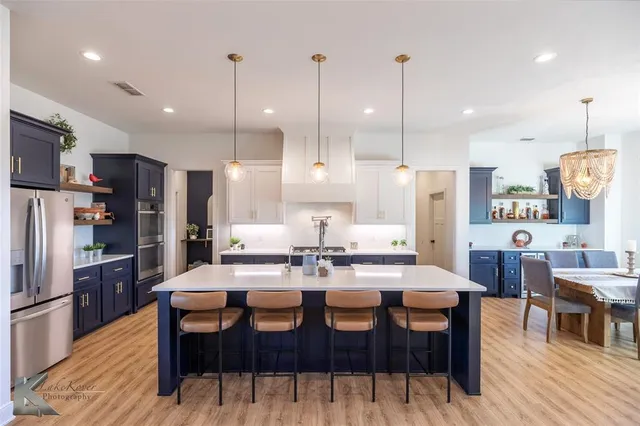 a kitchen with stainless steel appliances kitchen island granite countertop a dining table chairs and a refrigerator