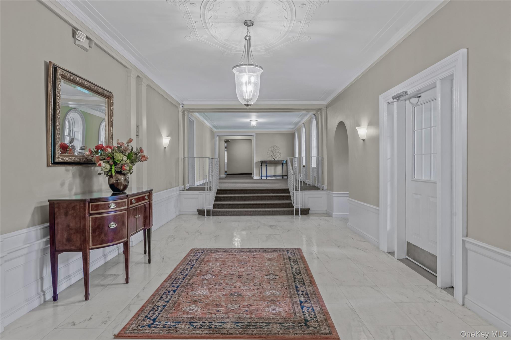 90 Knightsbridge Road, Unit 3N Great Neck, NY 11021 - Photo 3 of 16 a view of a hallway with wooden floor and a chandelier