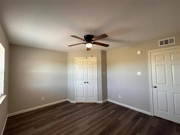 an empty room with wooden floor fan and windows