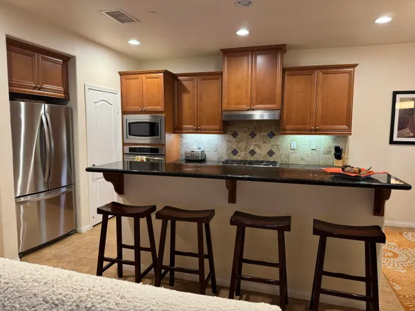 a kitchen with stainless steel appliances granite countertop a refrigerator a stove a sink a dining table and chairs with wooden floor