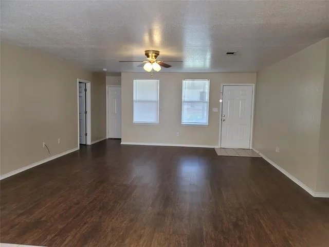 an empty room with wooden floor a chandelier fan and windows