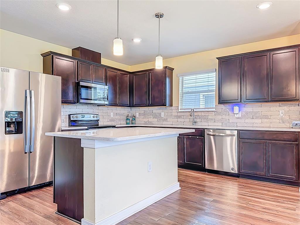 9324 Rally Spring Loop Wesley Chapel, FL 33545 - Photo 15 of 57 a kitchen with kitchen island granite countertop wooden floors stainless steel appliances a sink and a center island