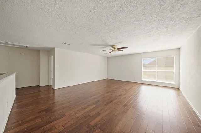 an empty room with wooden floor ceiling fan and windows