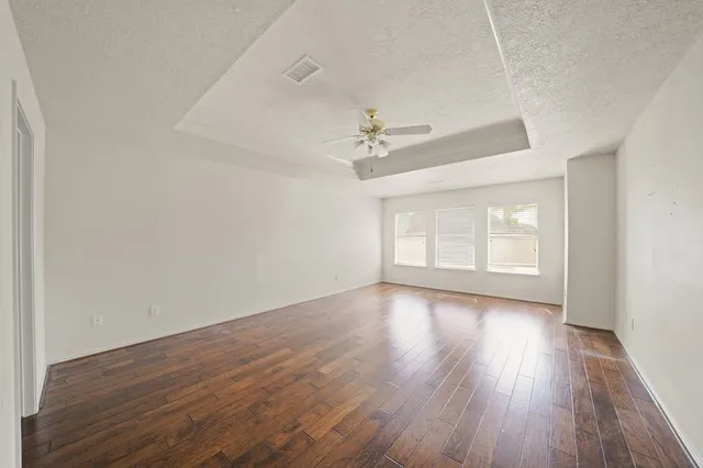 a view of an empty room with wooden floor and a ceiling fan