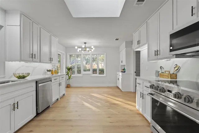 a kitchen with stainless steel appliances a stove top oven a sink a refrigerator white cabinets and wooden floor