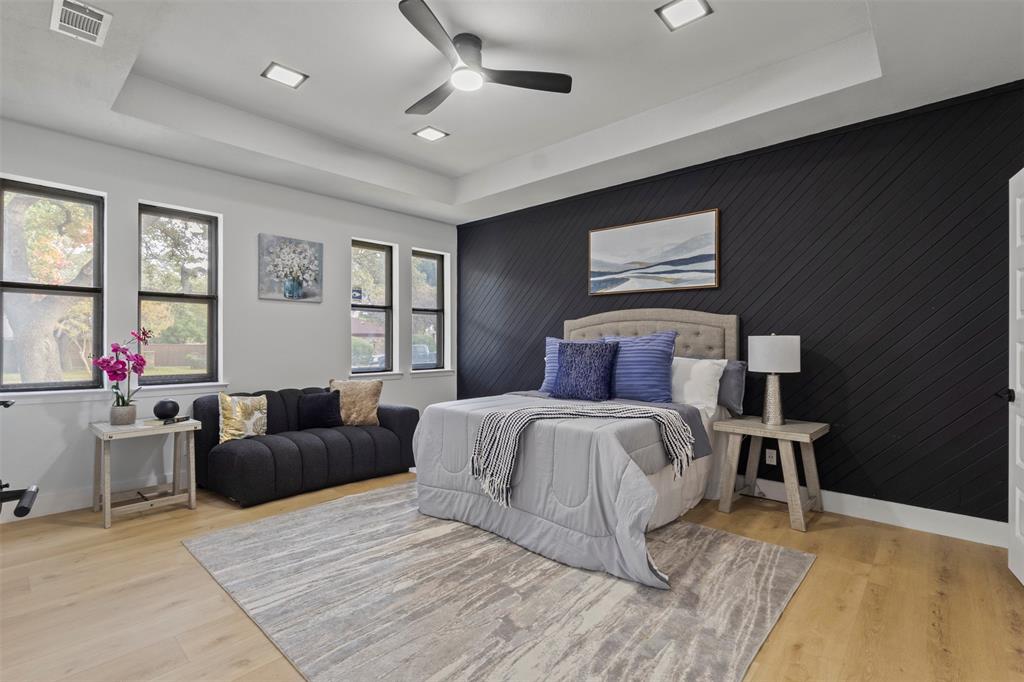 1 Spring Valley Court Richardson, TX 75081 - Photo 4 of 40 Bedroom featuring a tray ceiling, an accent wall, light wood-style flooring, ceiling fan, and wooden walls