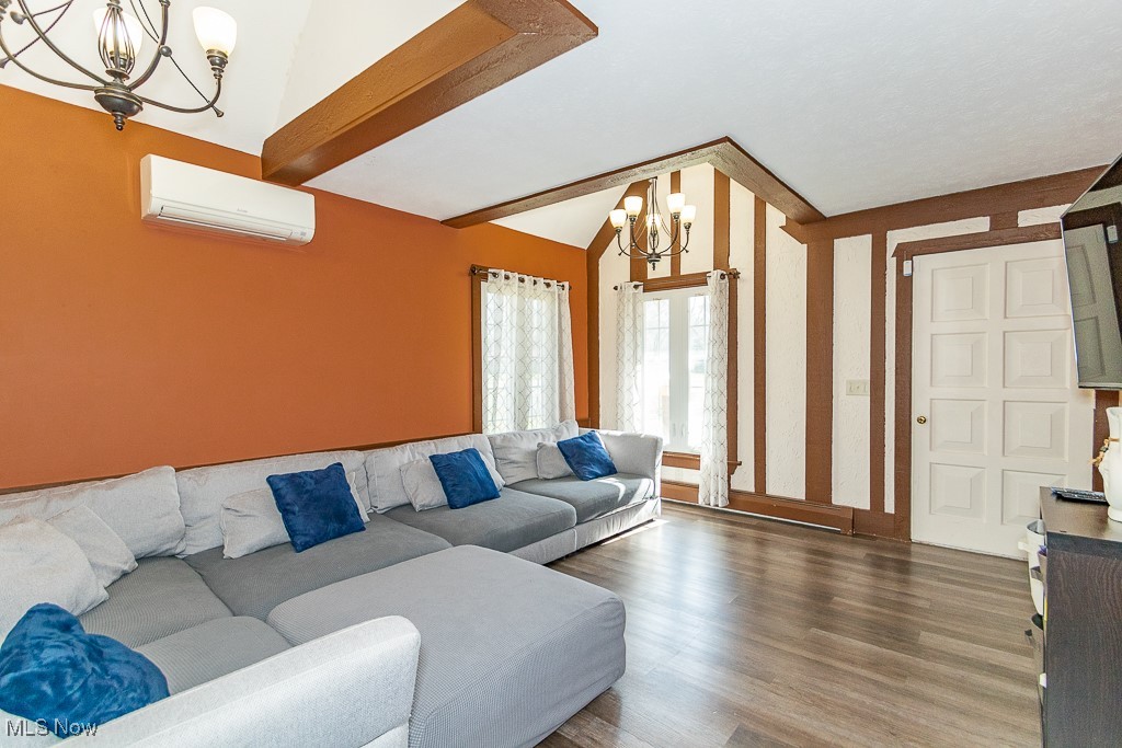 244 Barrington Ridge Road Painesville, OH 44077 - Photo 22 of 50 Living room featuring a notable chandelier, a wall mounted air conditioner, lofted ceiling with beams, and wood finished floors