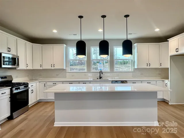 a kitchen with stainless steel appliances granite countertop a sink a stove a oven and white cabinets with wooden floor
