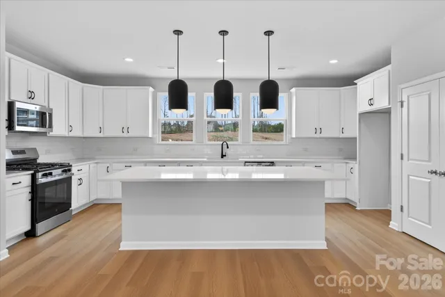 a kitchen with stainless steel appliances kitchen island granite countertop a sink a stove and white cabinets