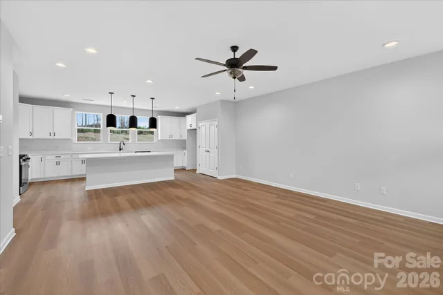 a large white kitchen with kitchen island a stove a sink dishwasher and white cabinets with wooden floor