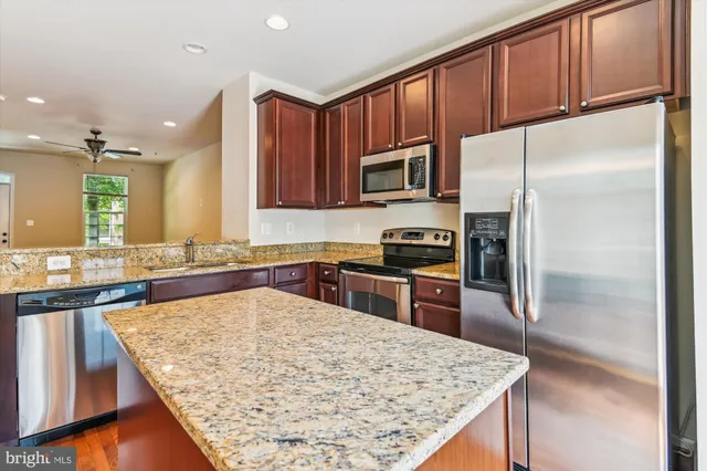 a kitchen with stainless steel appliances granite countertop a refrigerator a stove and a sink with wooden cabinets