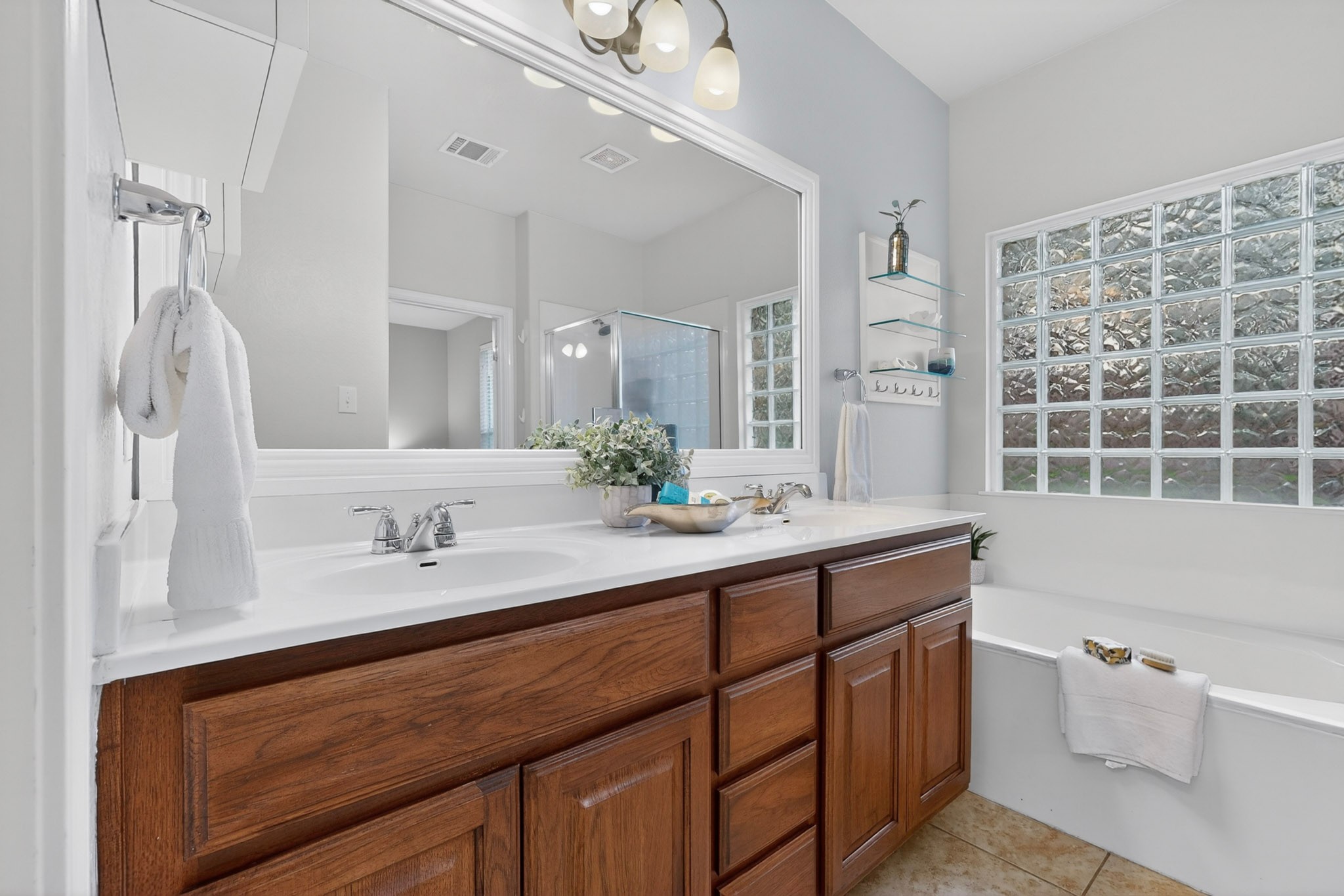 178 Limestone Trail Austin, TX 78737 - Photo 23 of 40 Double vanity with undermount sinks and chrome fixtures, ample storage within wood-finish cabinetry, a large framed mirror, and a soaking tub with an adjacent glass block window
