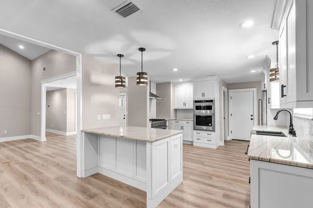 a large kitchen with stainless steel appliances kitchen island a large counter top and wooden floors