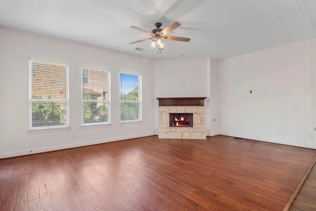 an empty room with wooden floor fan and windows