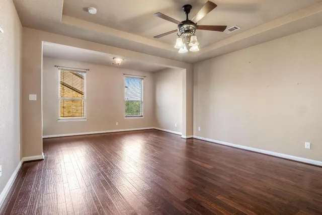 an empty room with wooden floor chandelier fan and windows