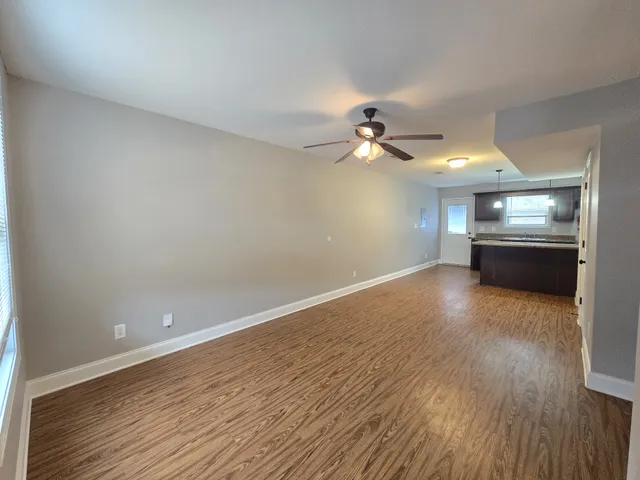 an empty room with wooden floor chandelier fan and windows