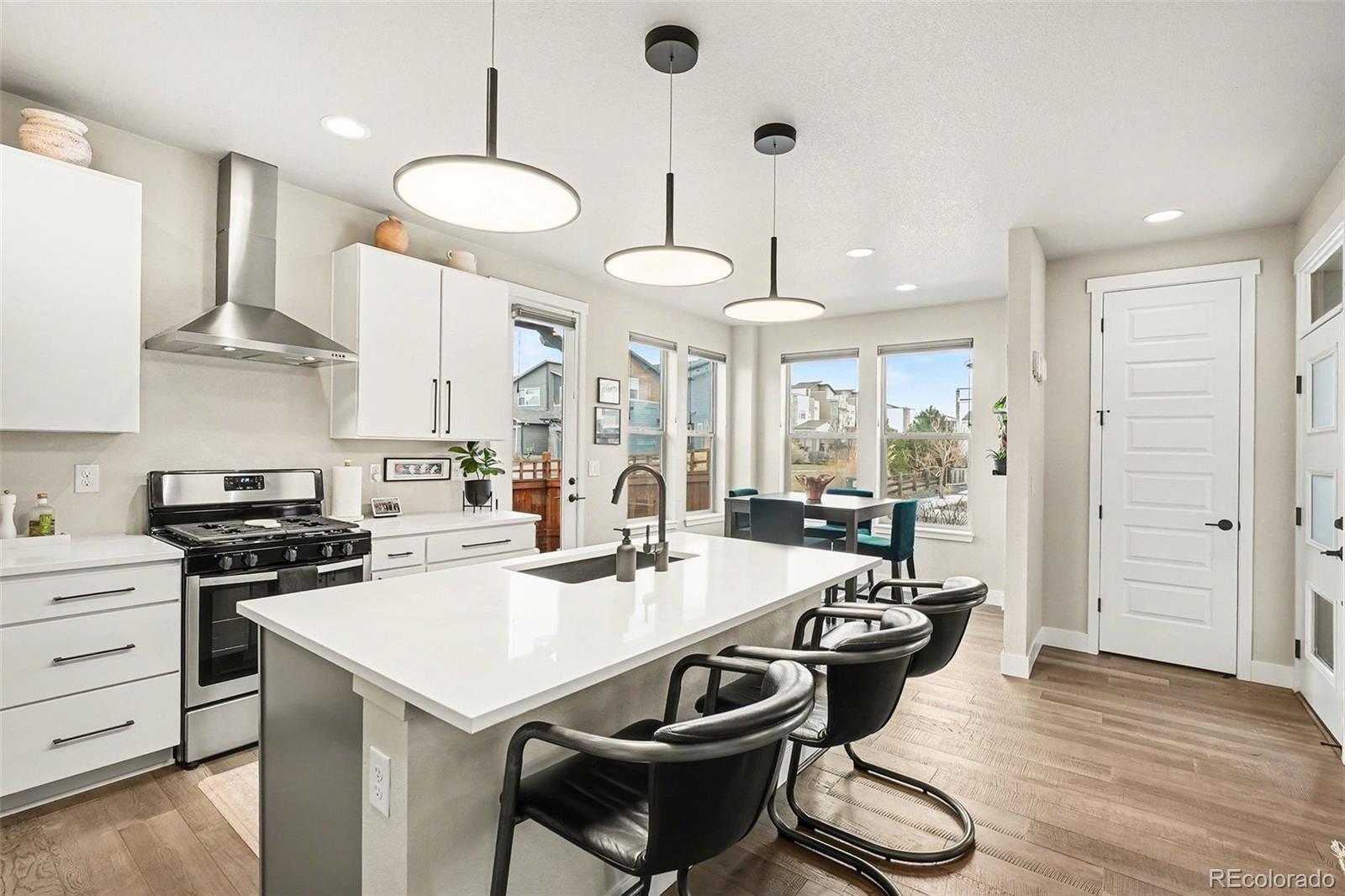 6793 Canosa Street Denver, CO 80221 - Photo 9 of 34 a kitchen with stainless steel appliances a stove a sink a dining table and chairs with wooden floor