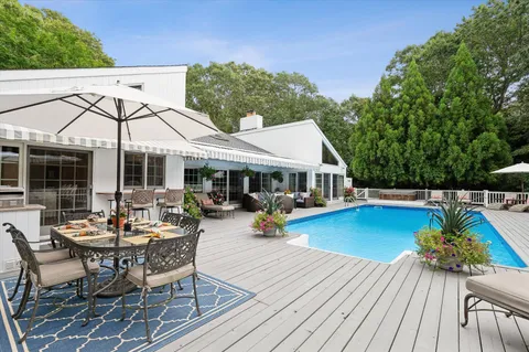 a view of a patio with dining table and chairs under an umbrella with wooden floor