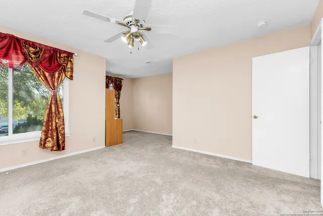 an empty room with a chandelier fan and windows
